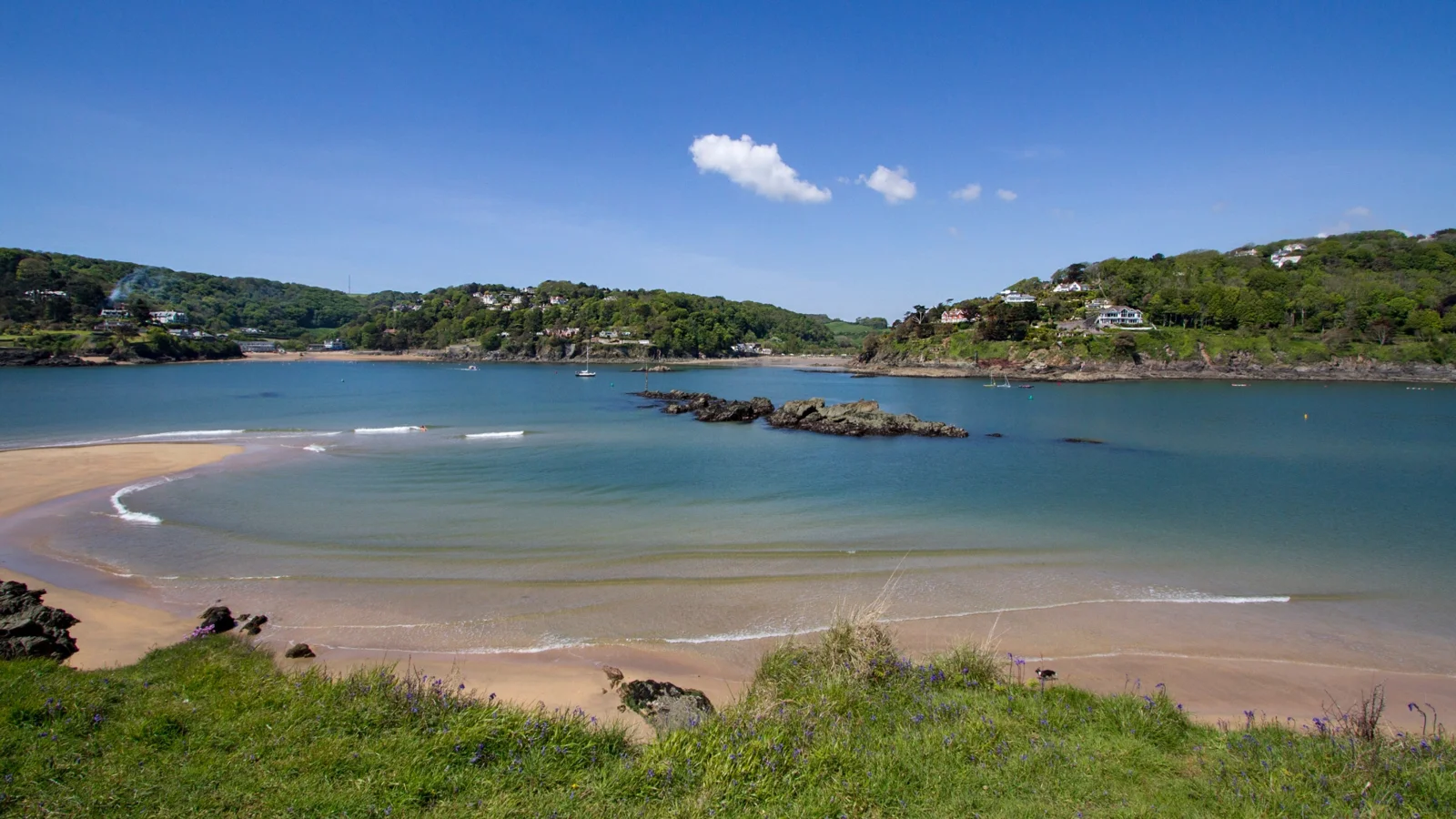 Sand and blue estuary water at Mill Bay with wooded slopes beyond