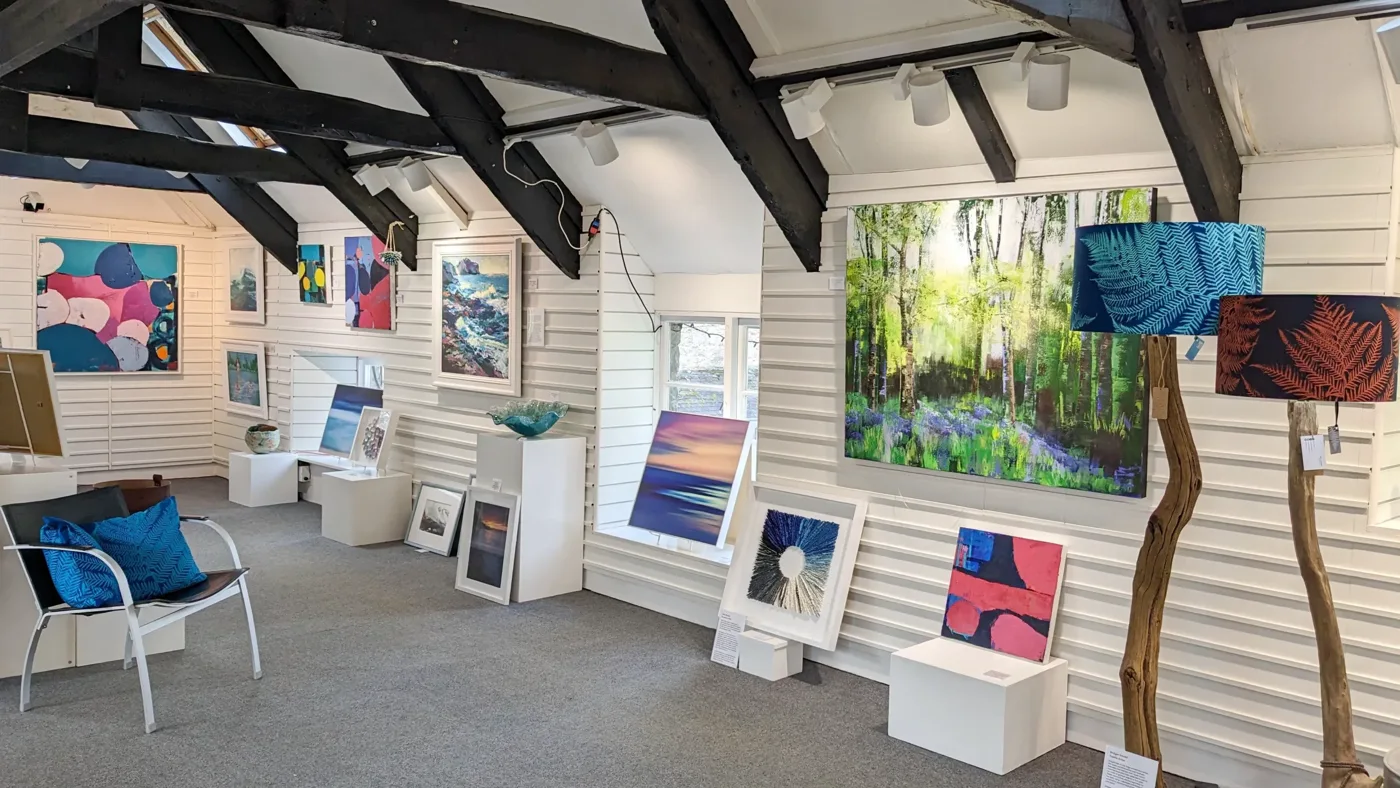 Paintings displayed beneath dark roof beams in Mooch’s upper gallery