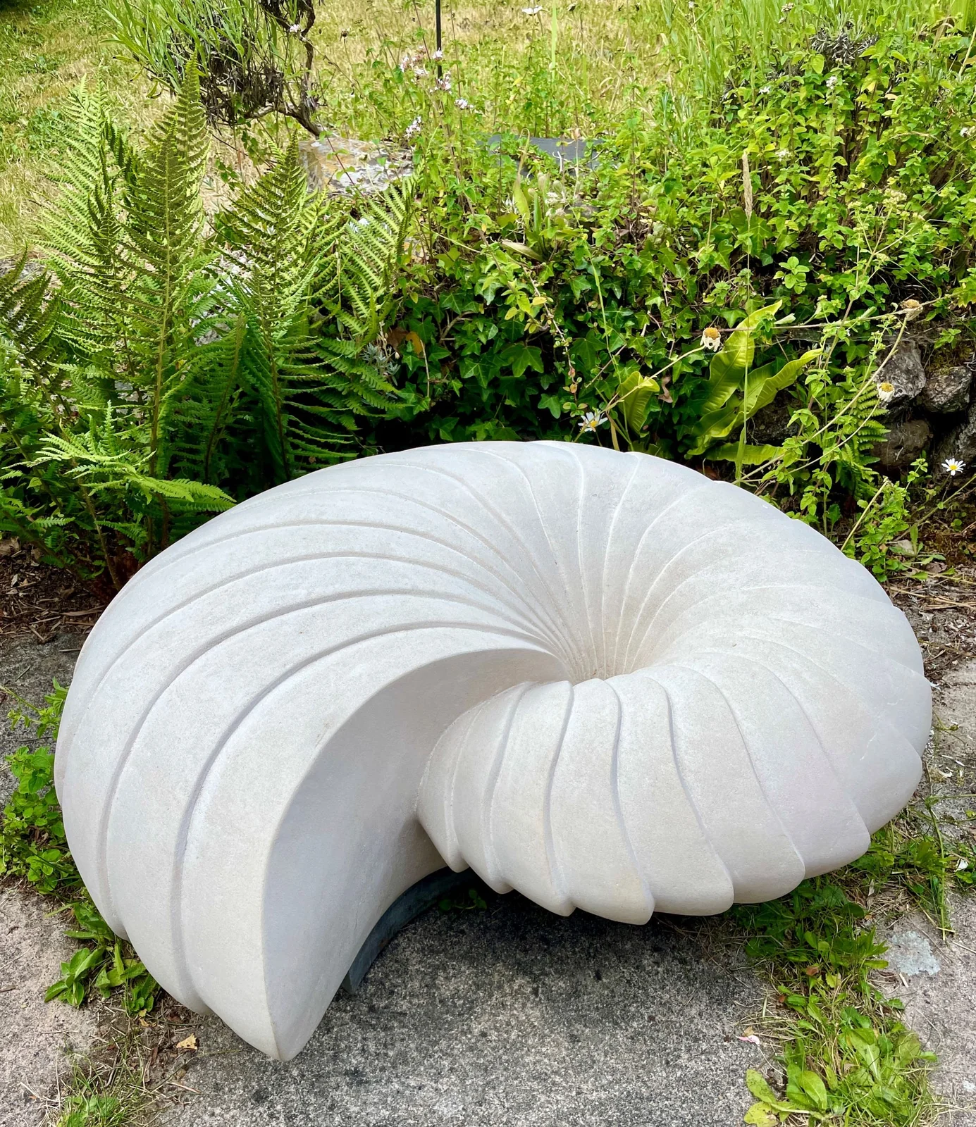 White stone shell sculpture among garden plants