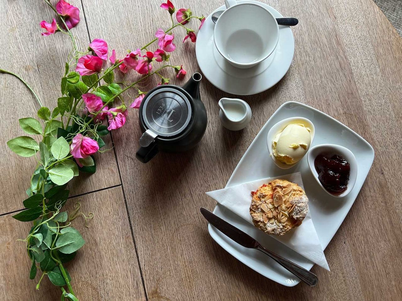 Cream tea and pink flowers on a wooden table at Oak Barn