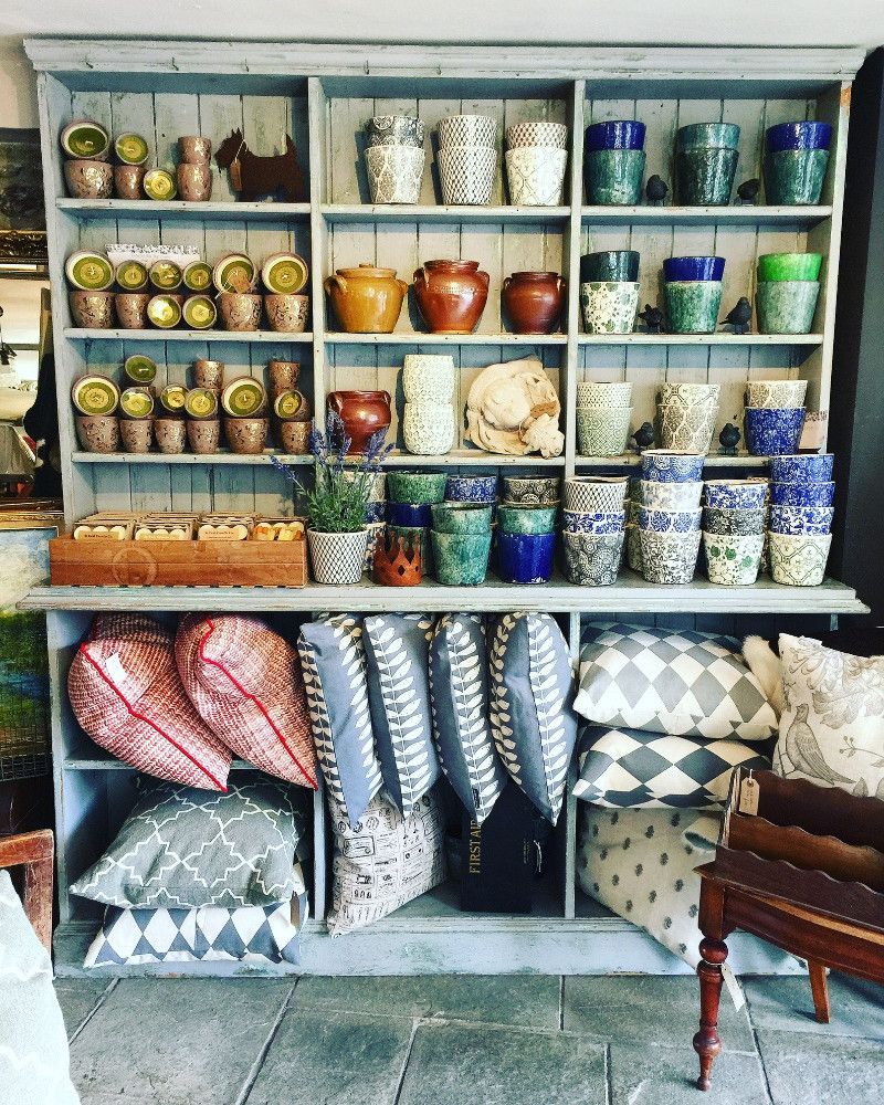 Colourful cups, candles and patterned cushions on pale painted shelves