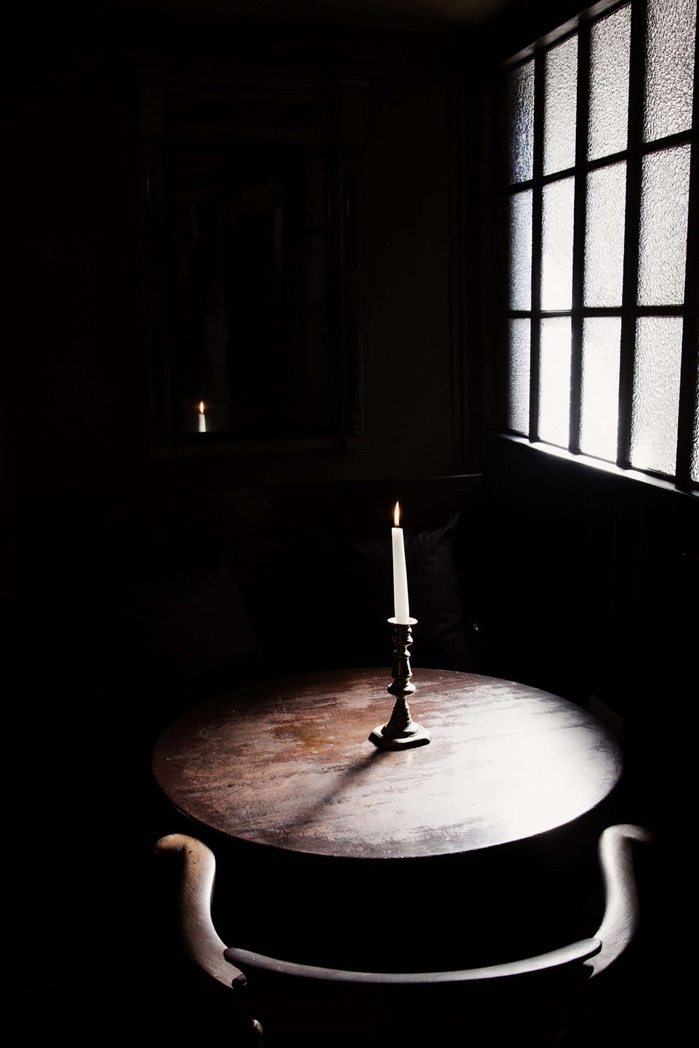 A small round table and single candle beside a leaded window