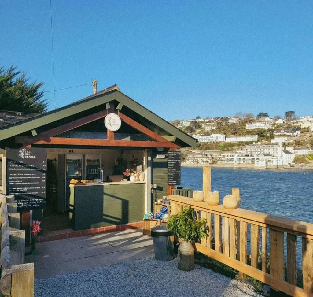 Small green café building beside a wooden railing above the estuary