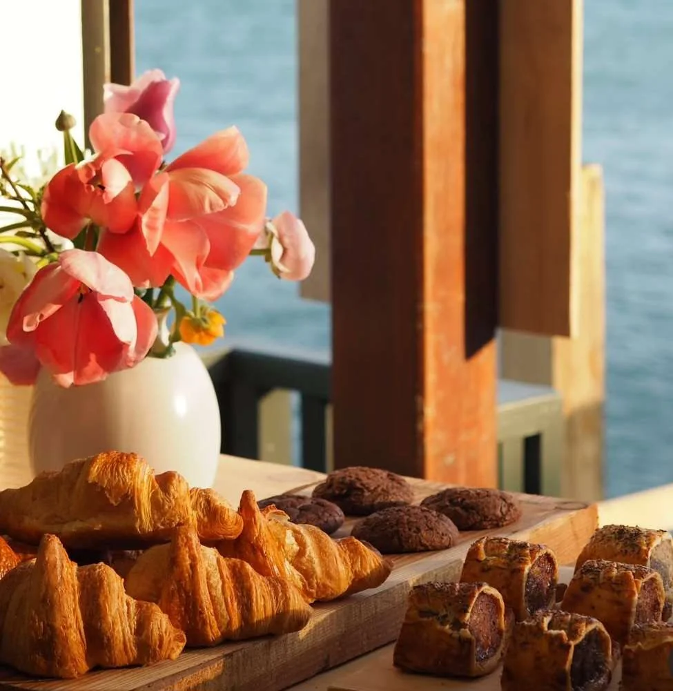 Pastries displayed beside flowers at a window overlooking the water