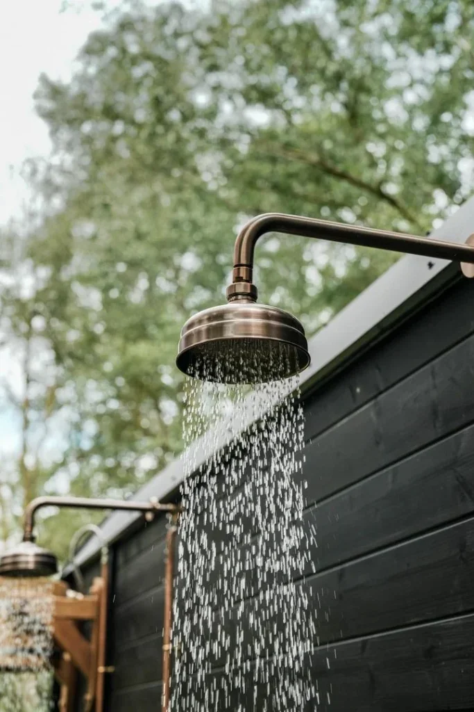 Outdoor shower beside a dark timber building and leafy trees