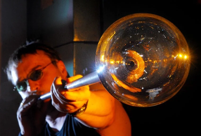 Glassmaker shaping a glowing glass vessel on a blowing iron