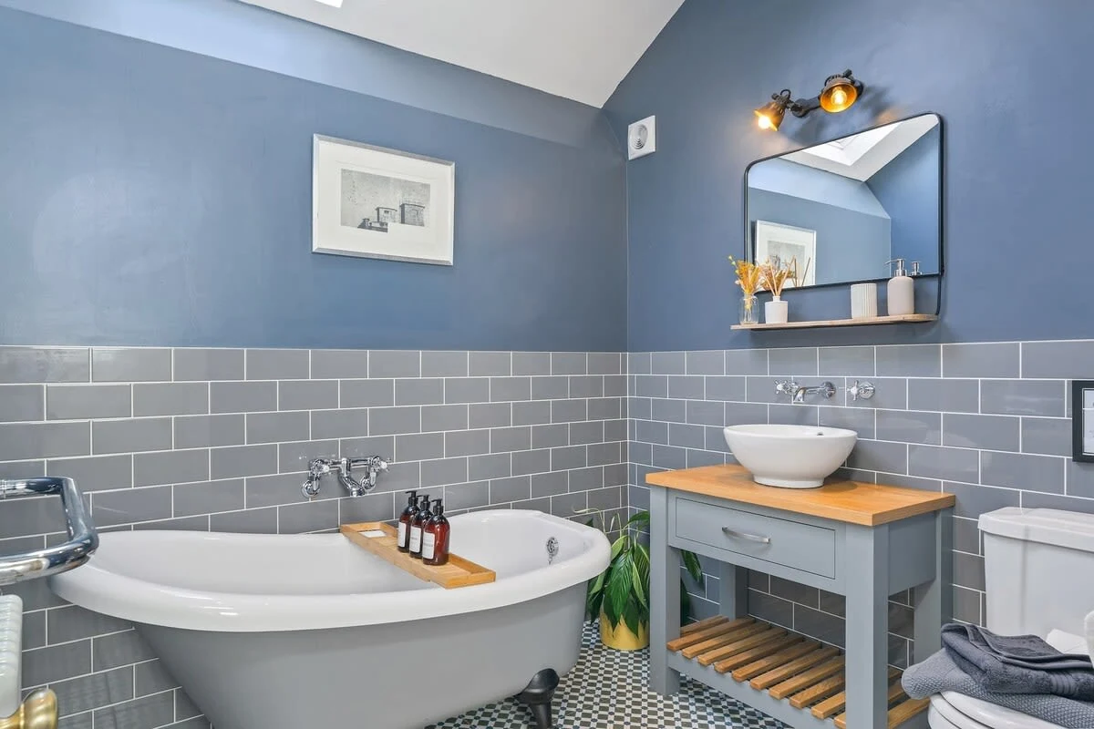 Freestanding bath beneath a blue wall with grey tiled splashback