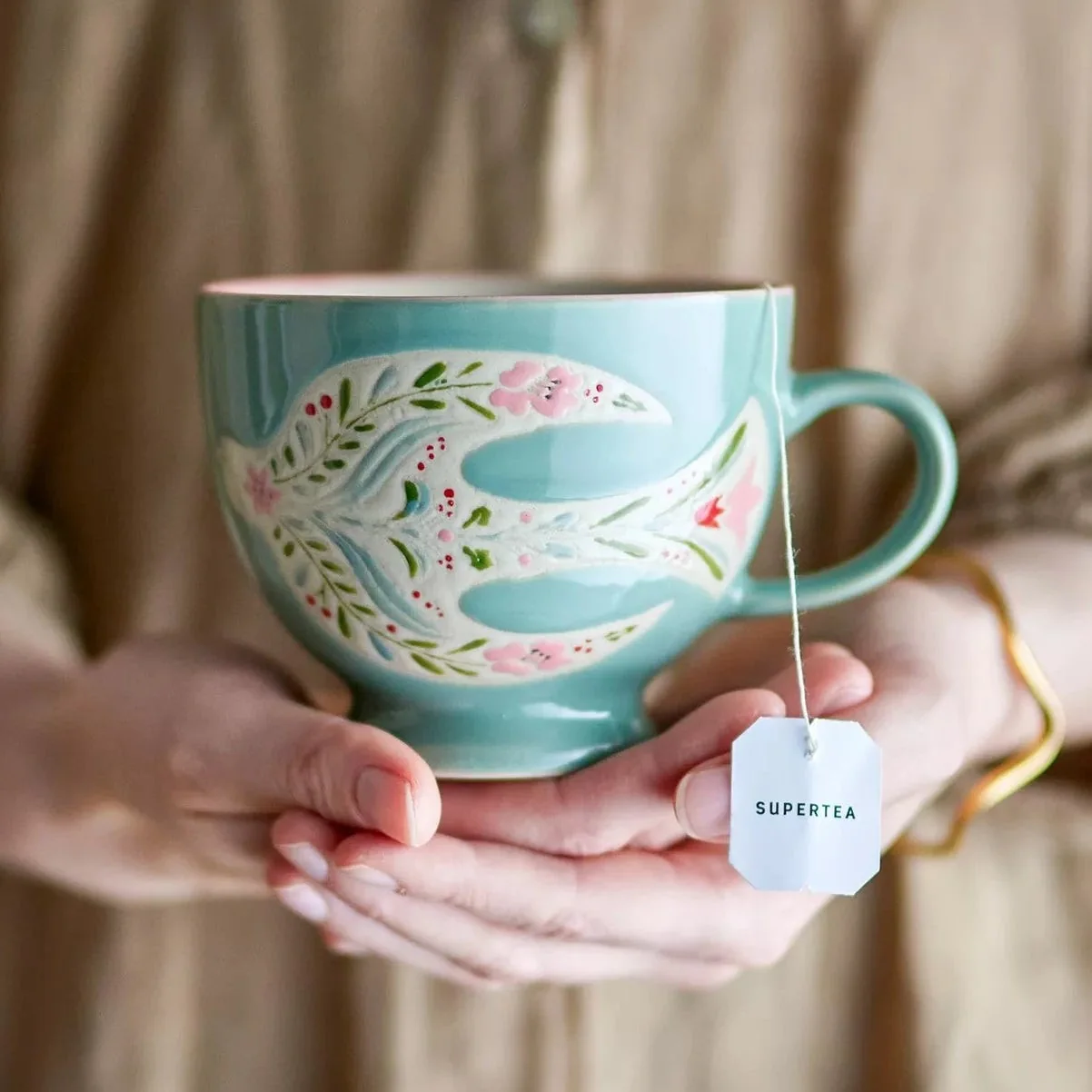 A turquoise floral mug held in two hands