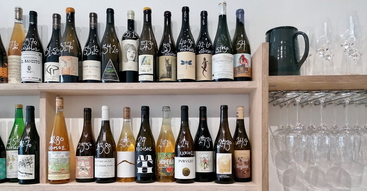 Natural wine bottles on pale wooden shelves at Pullo