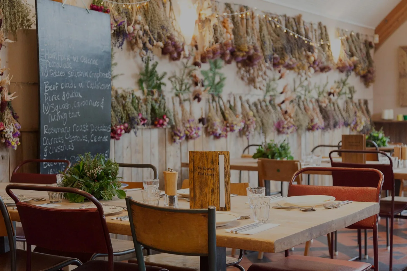 Dining room with dried flowers and mismatched chairs at Riverford Field Kitchen