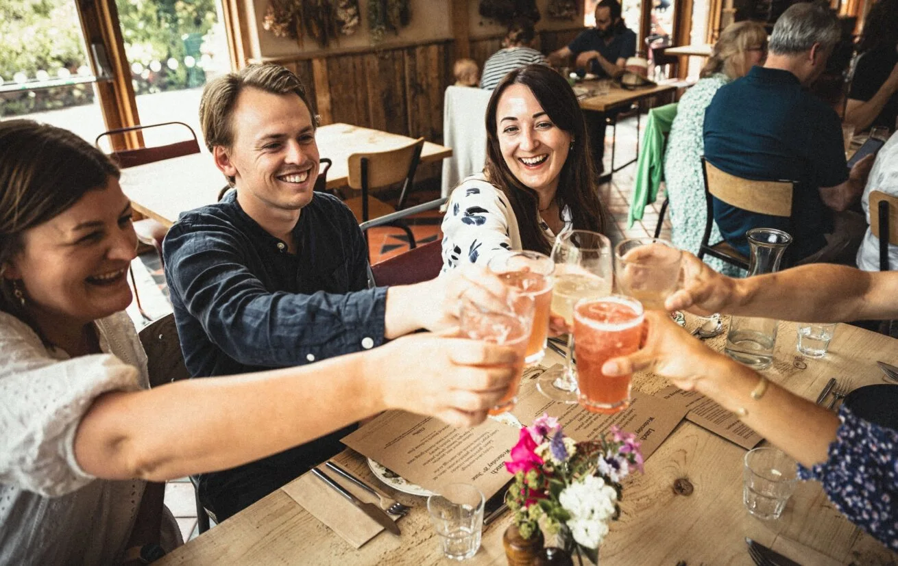 Friends raising drinks around a Riverford Field Kitchen table