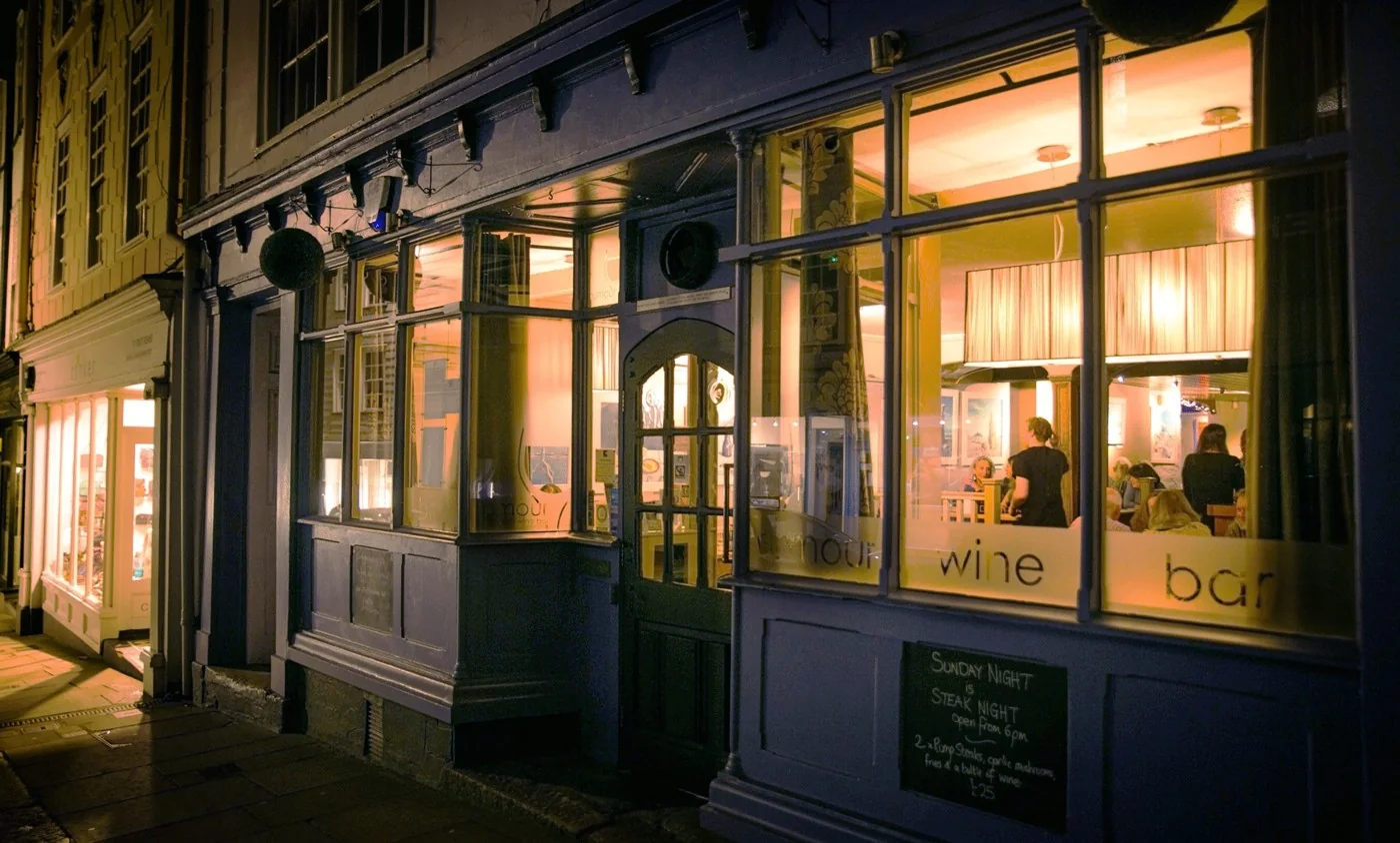Rumour’s blue shopfront glowing warmly after dark on Totnes High Street