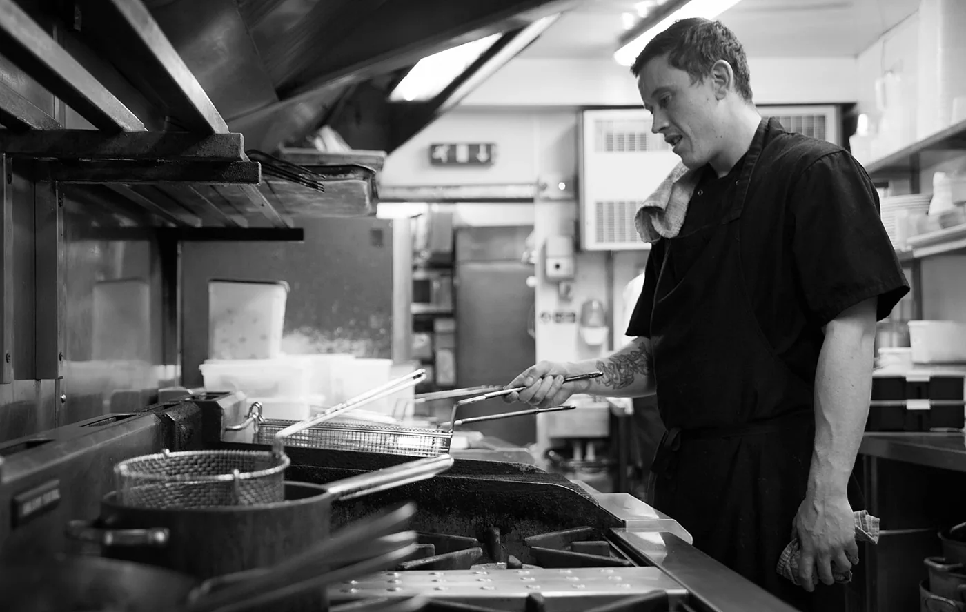 A chef cooking beneath timber beams in Rumour’s kitchen