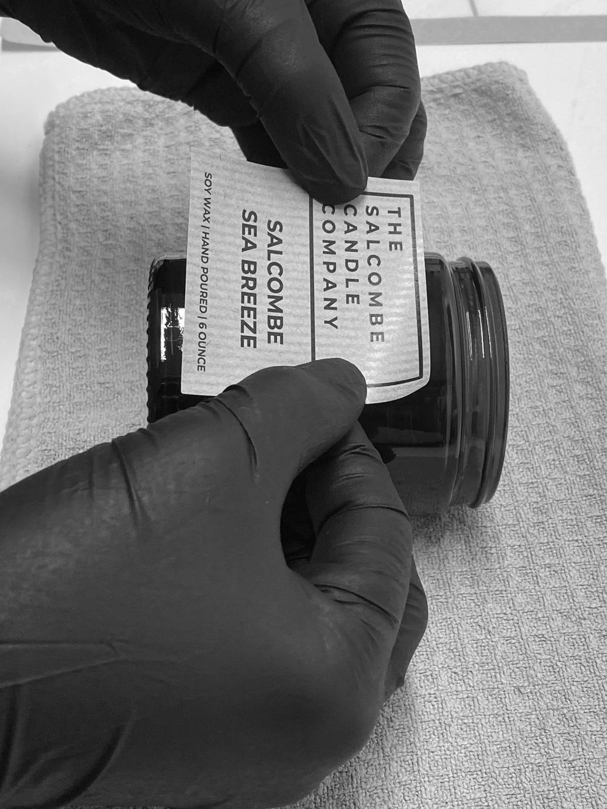 Hands applying a Salcombe Candle Company label to a jar