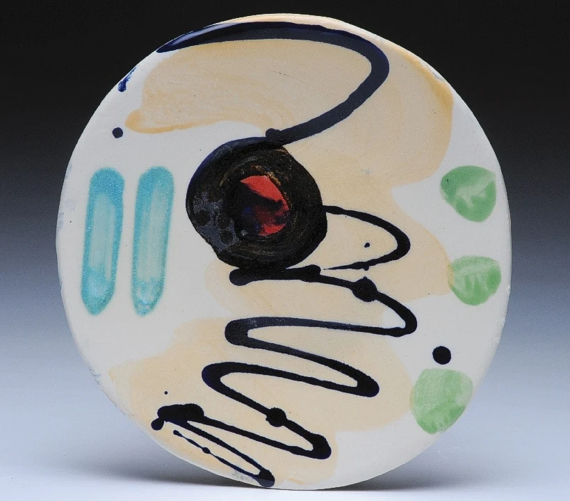 A ceramic plate painted with loose navy lines and turquoise and green shapes by Sandy Brown