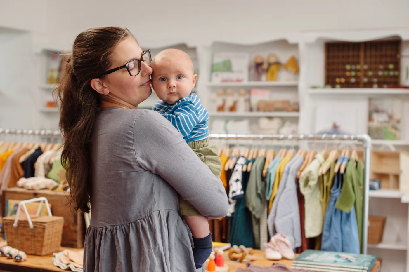 Woman holding a child inside SMALL-FOLK among children’s clothing displays
