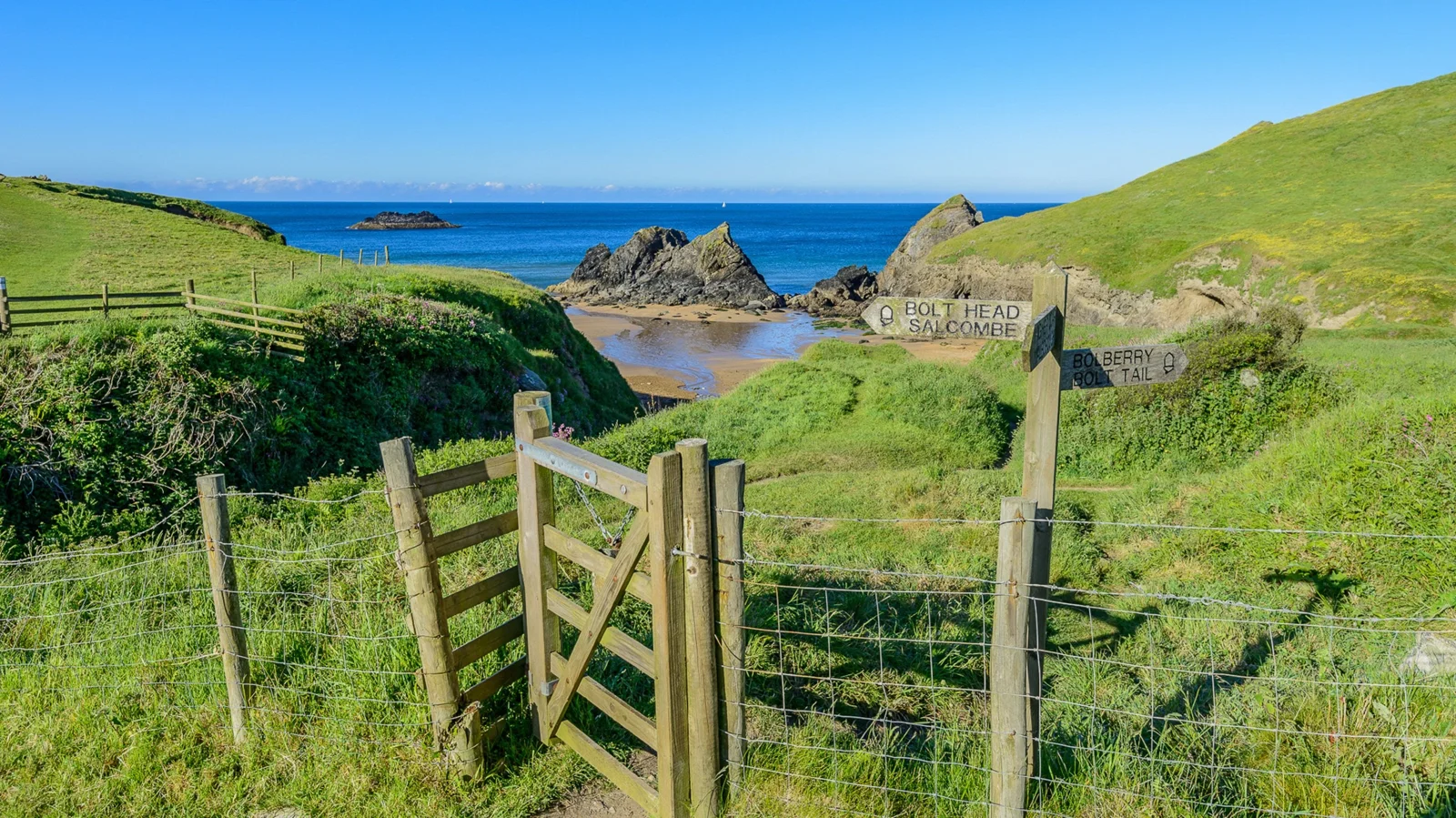 Gate opening towards green fields and the rocky mouth of Soar Mill Cove