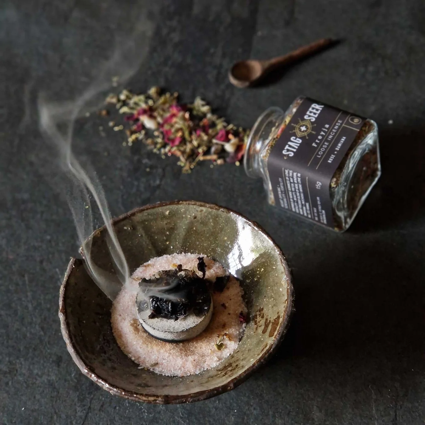 Loose incense, a ceramic burning bowl and smoke beside a Stag + Seer bottle