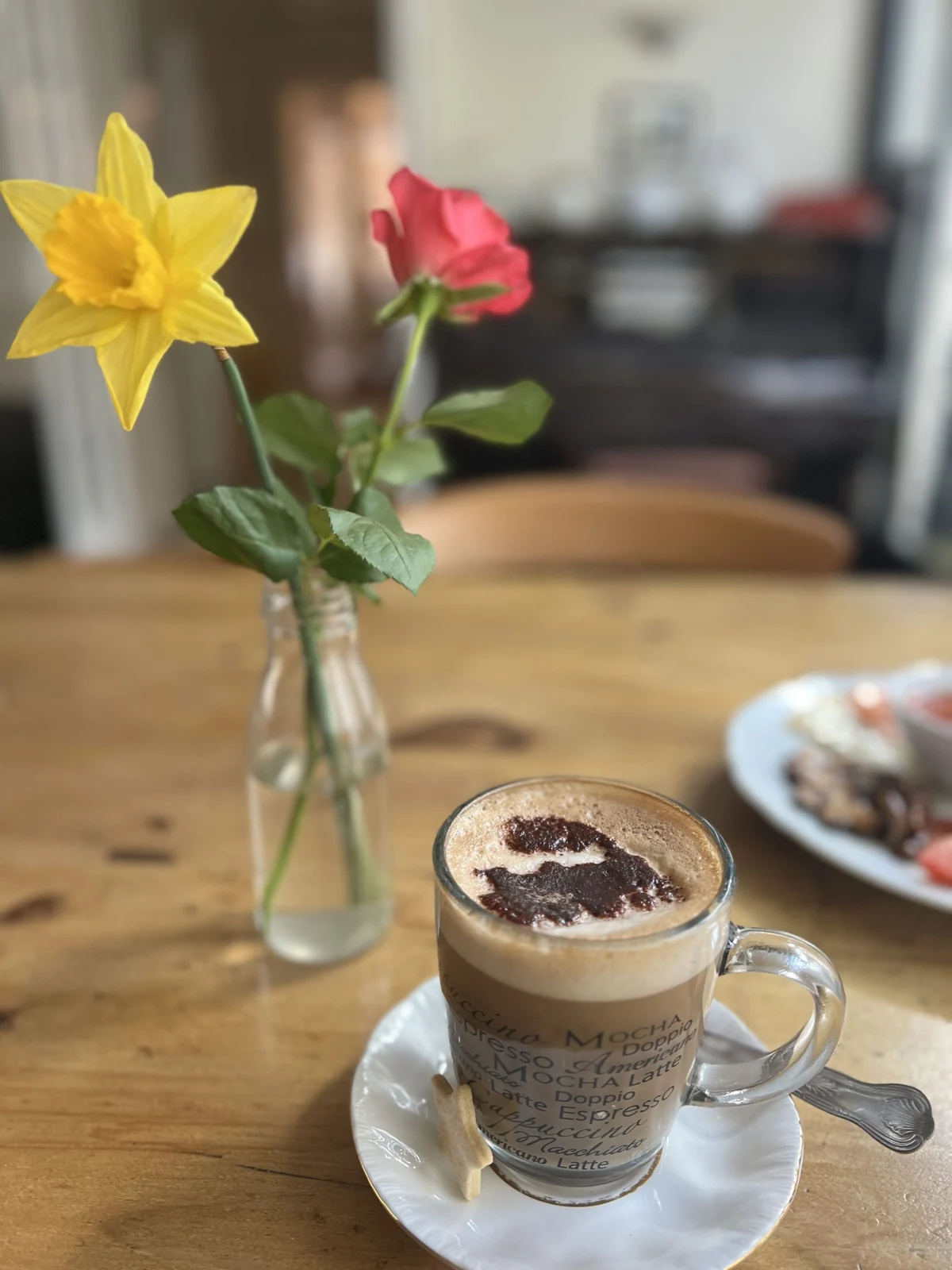 A cappuccino beside flowers on a wooden café table at Station House