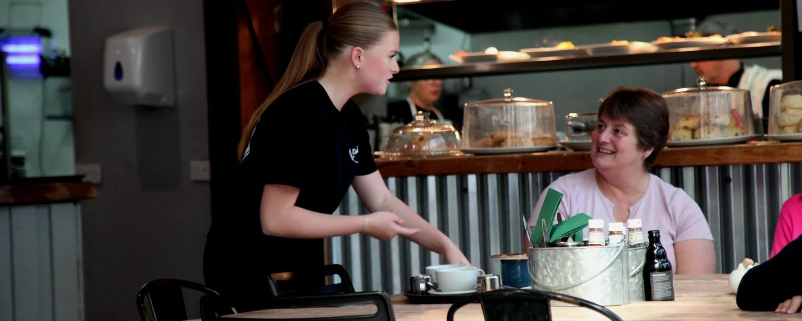 A member of staff serving a seated café customer