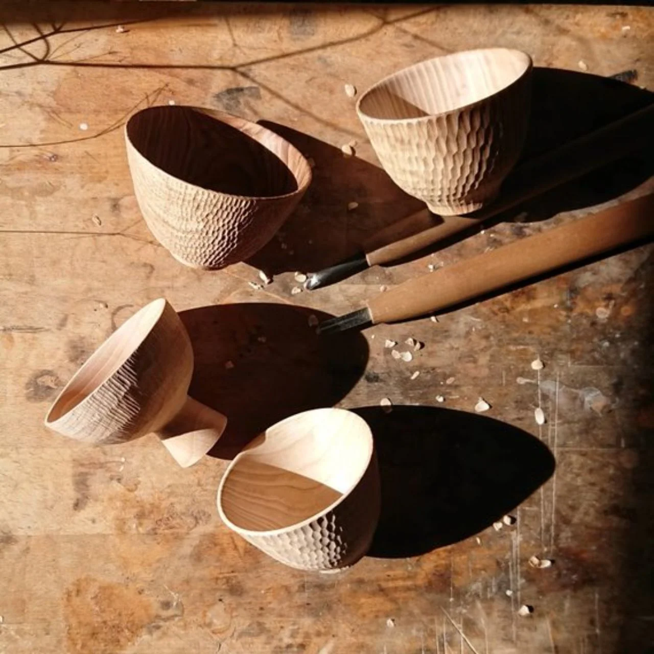 Wooden bowls and carving tools on a sunlit workbench