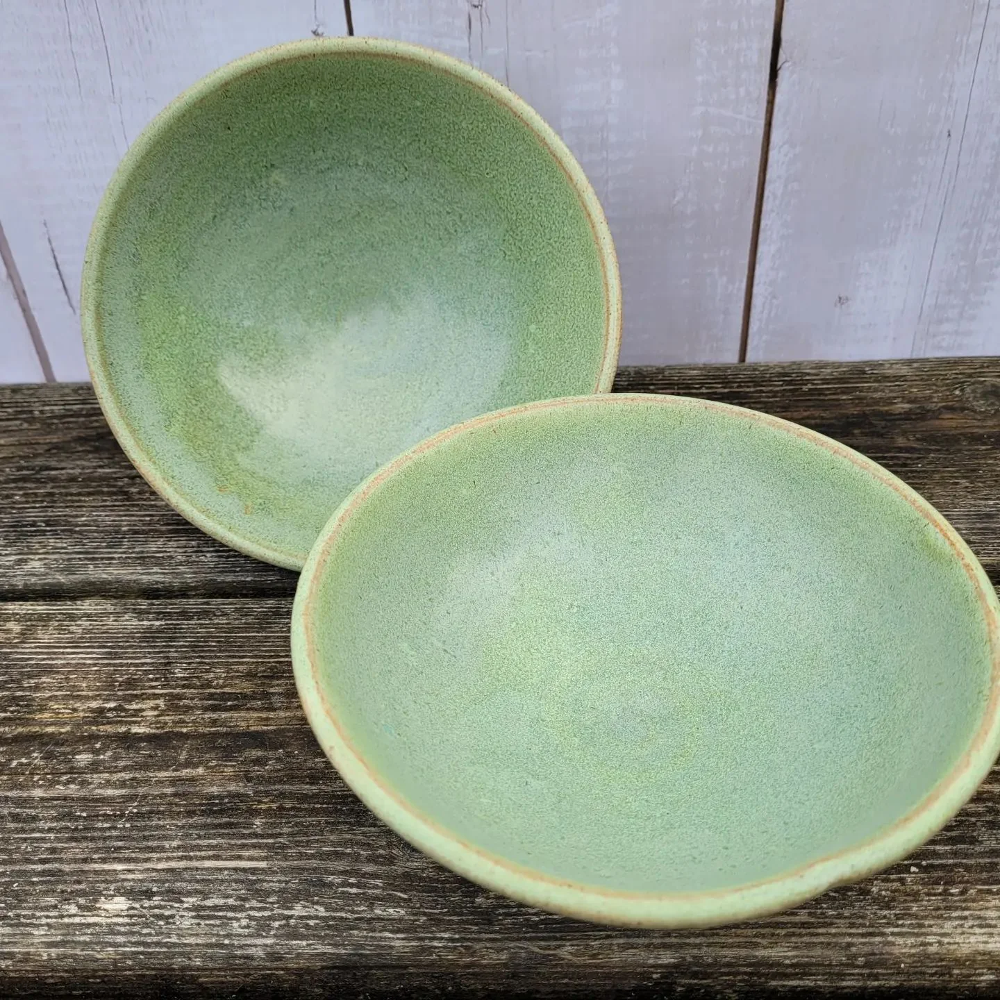 Two softly green glazed ceramic bowls on a wooden surface
