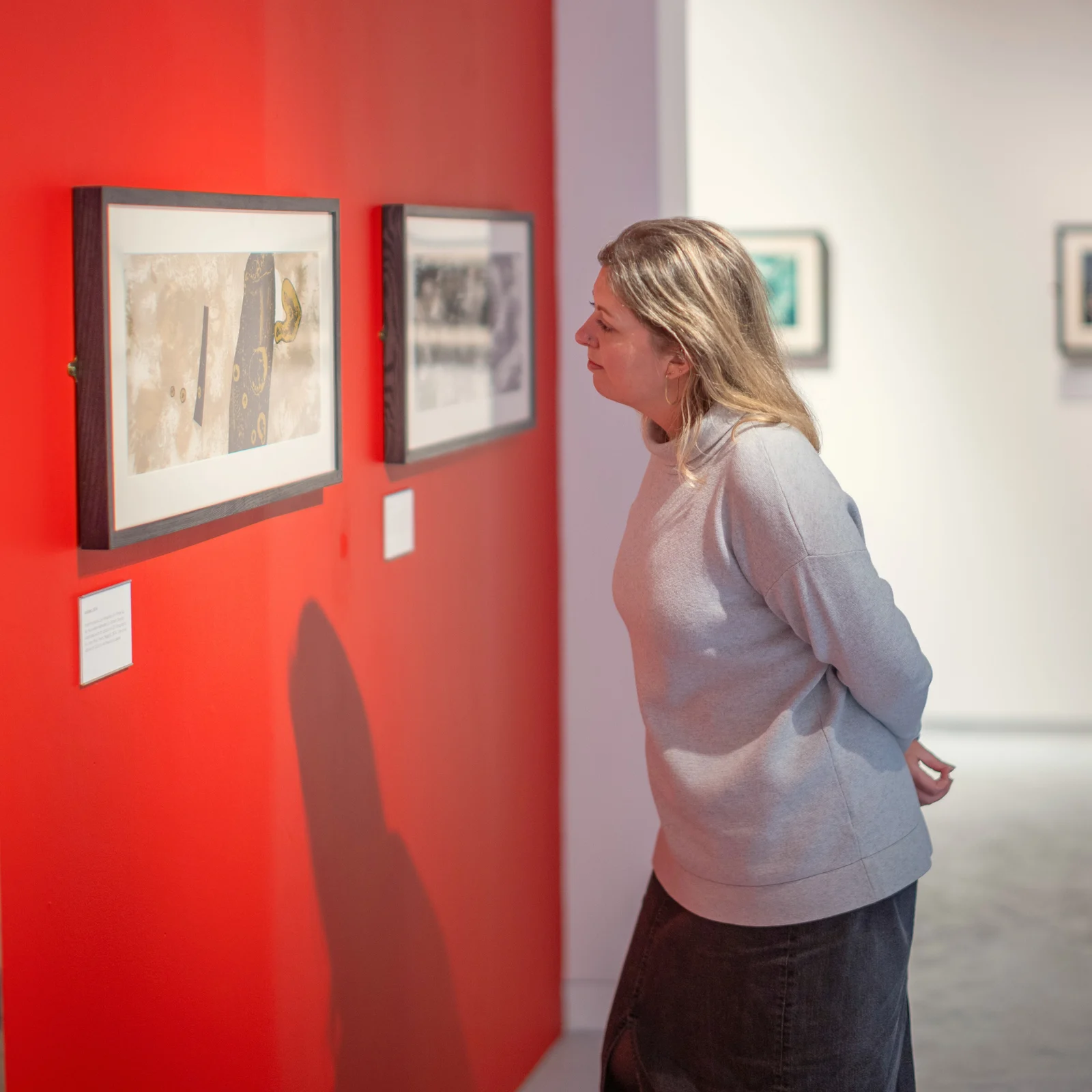 A visitor looking at framed artwork against a red gallery wall