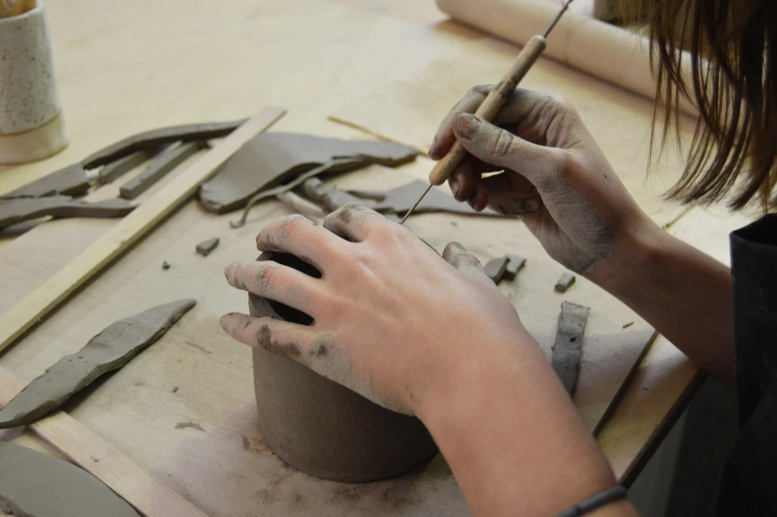 Hands shaping and decorating a clay vessel