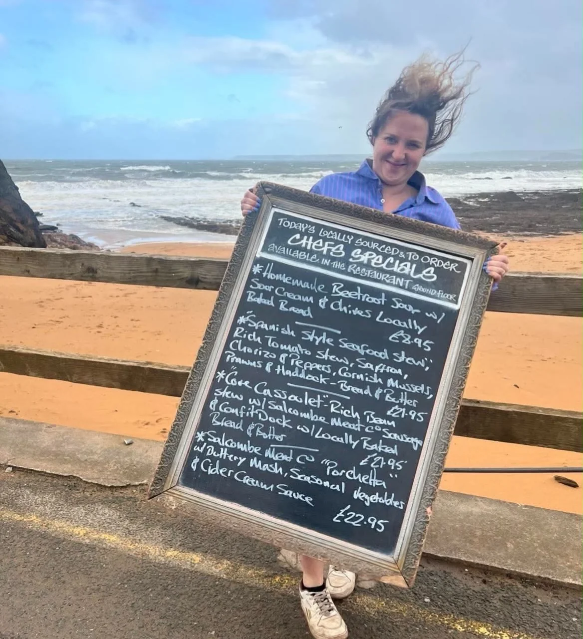 A member of The Cove team holding a specials board beside the beach