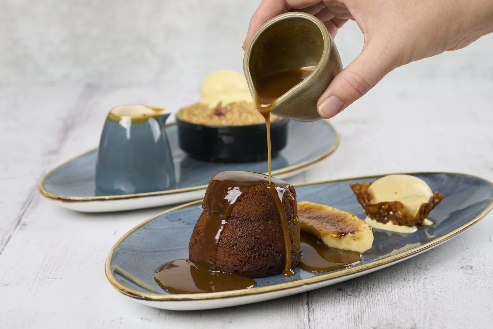 Sauce being poured over a pudding with ice cream