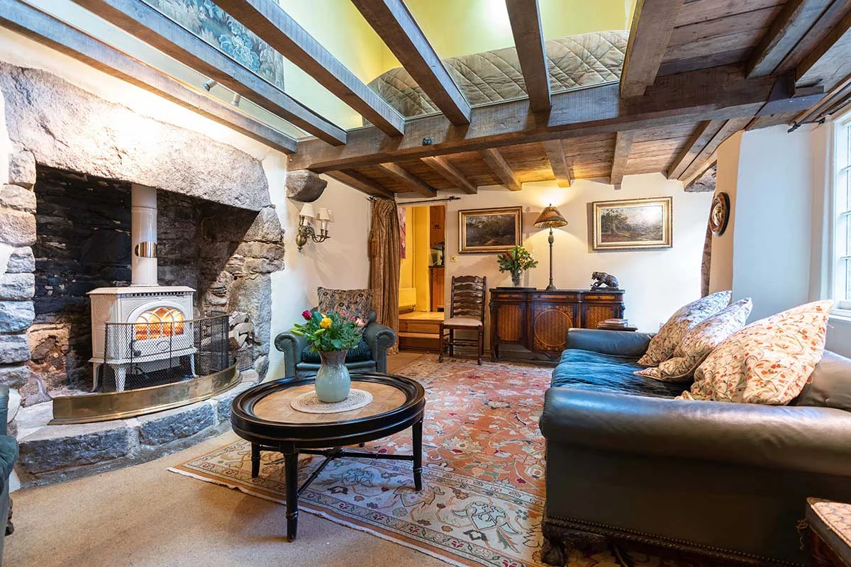 Beamed sitting room with a stone fireplace, patterned rug and dark leather sofas