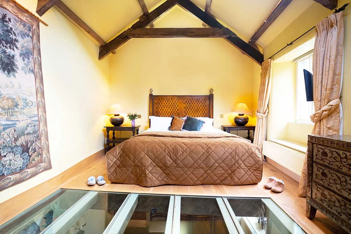 Yellow master bedroom with exposed beams, tapestry and a section of glass floor