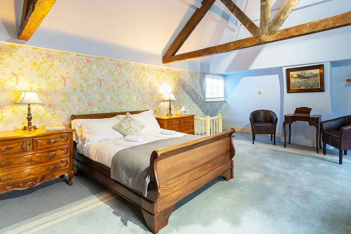 Wooden sleigh bed beneath exposed roof beams and floral wallpaper