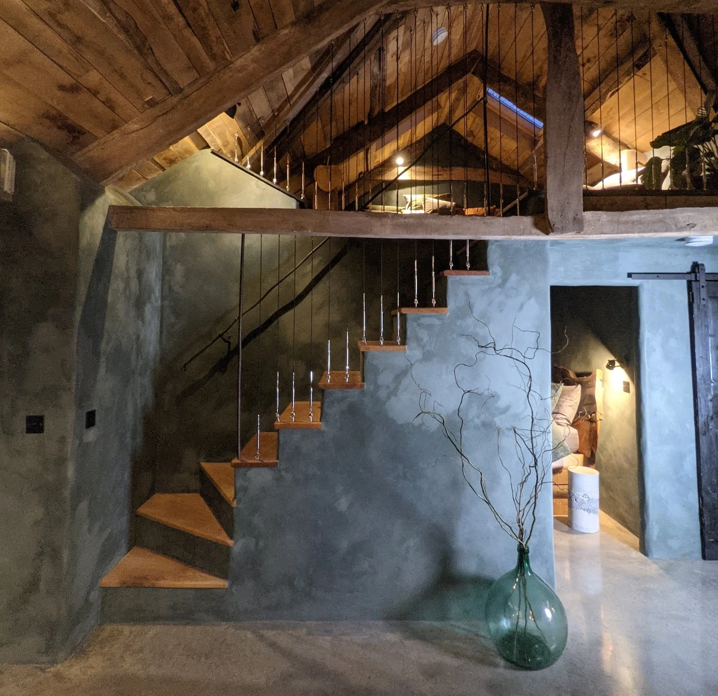 Exposed timber roof and stairs beside curved green walls in the converted barn
