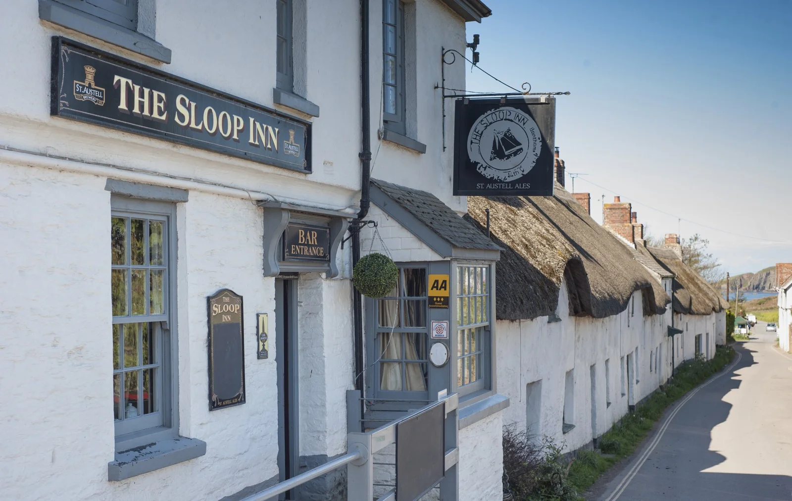 The Sloop Inn sign with thatched cottages along the road