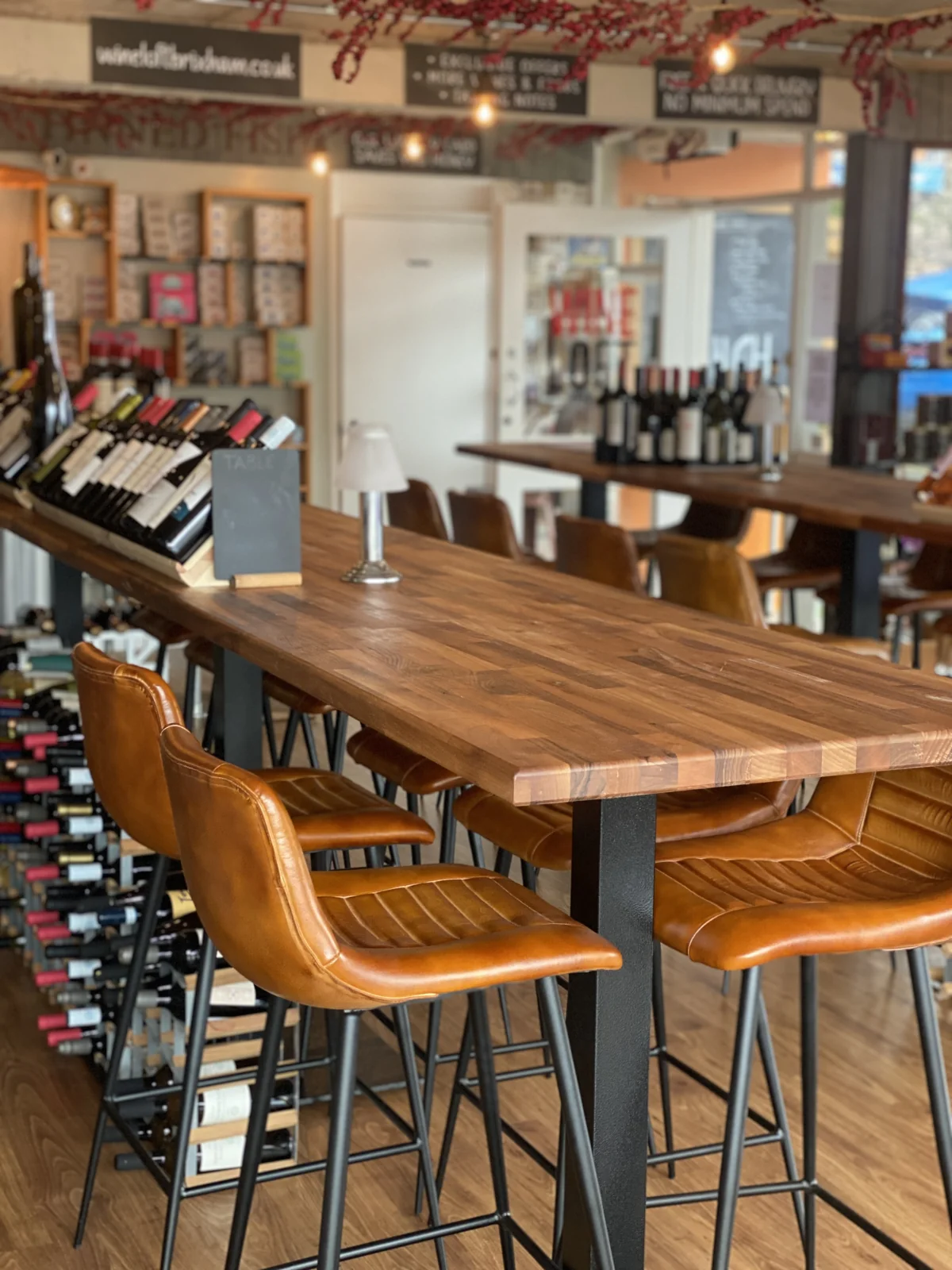 Wooden tables and chairs in The Wine Loft with bottles along the walls