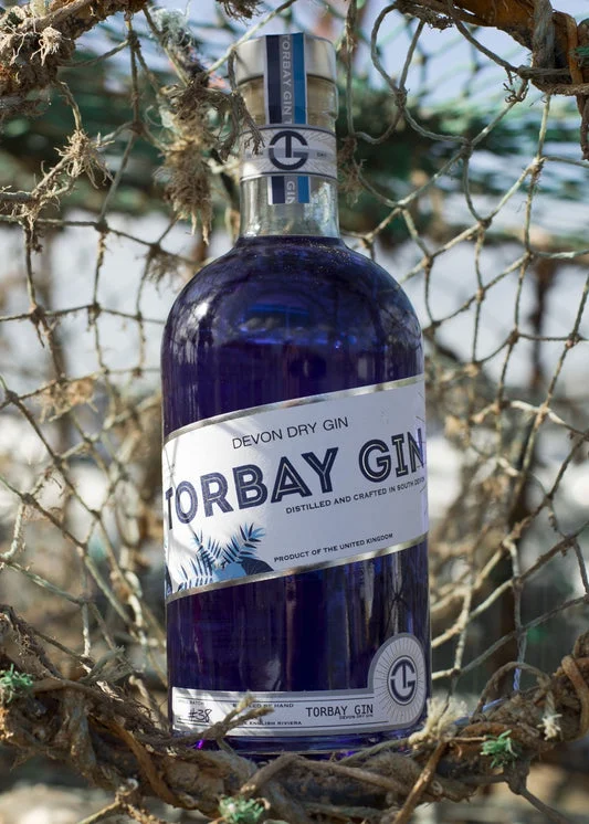A bottle of blue Torbay Gin hanging against harbour fishing nets