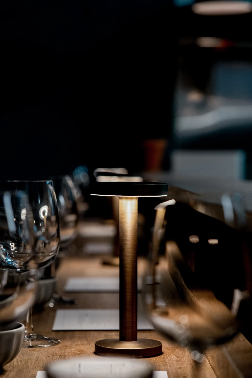 A glowing table lamp beside glasses and place settings at Verse