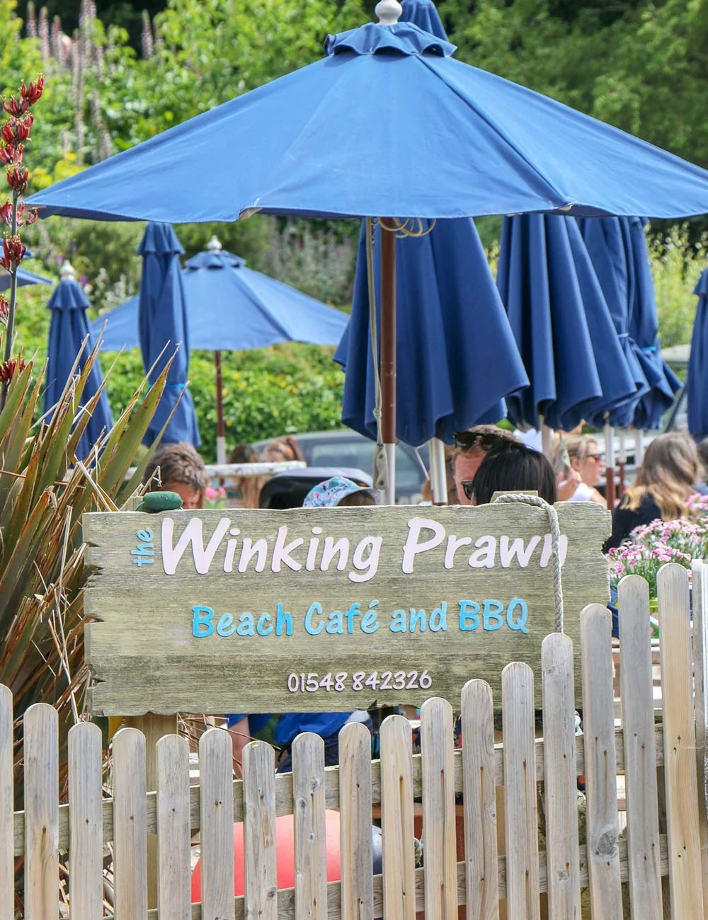 Winking Prawn garden entrance with blue parasols and white fence